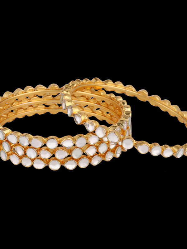 Gold bangles with white cabochon insets, stacked on a black background
