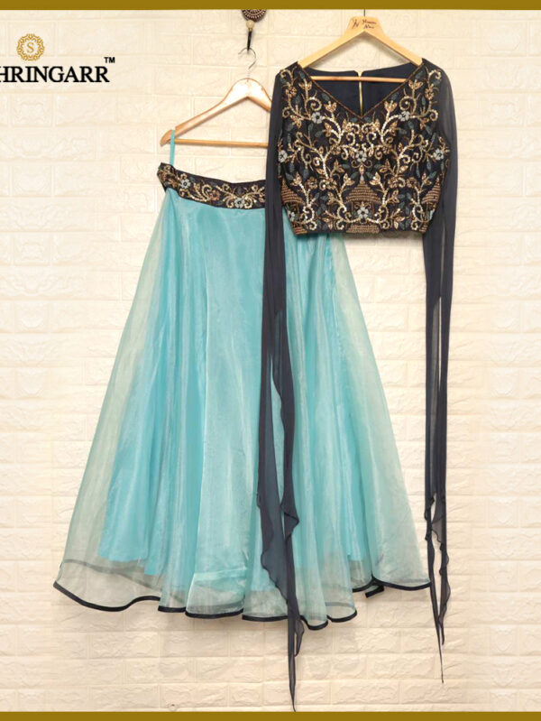 Turquoise lehenga with a black embellished blouse and matching navy dupatta on hangers against a beige brick wall.