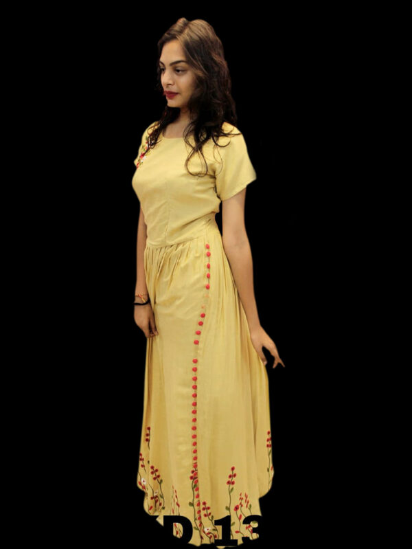 Woman wearing a pale yellow, full-length dress with red floral embroidery, standing against a black background.