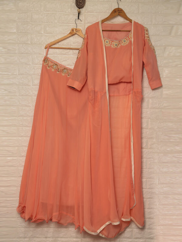 Peach traditional Indian outfit on hangers: embroidered neckline, sheer flowing dupatta, and matching pants against a white tiled wall.