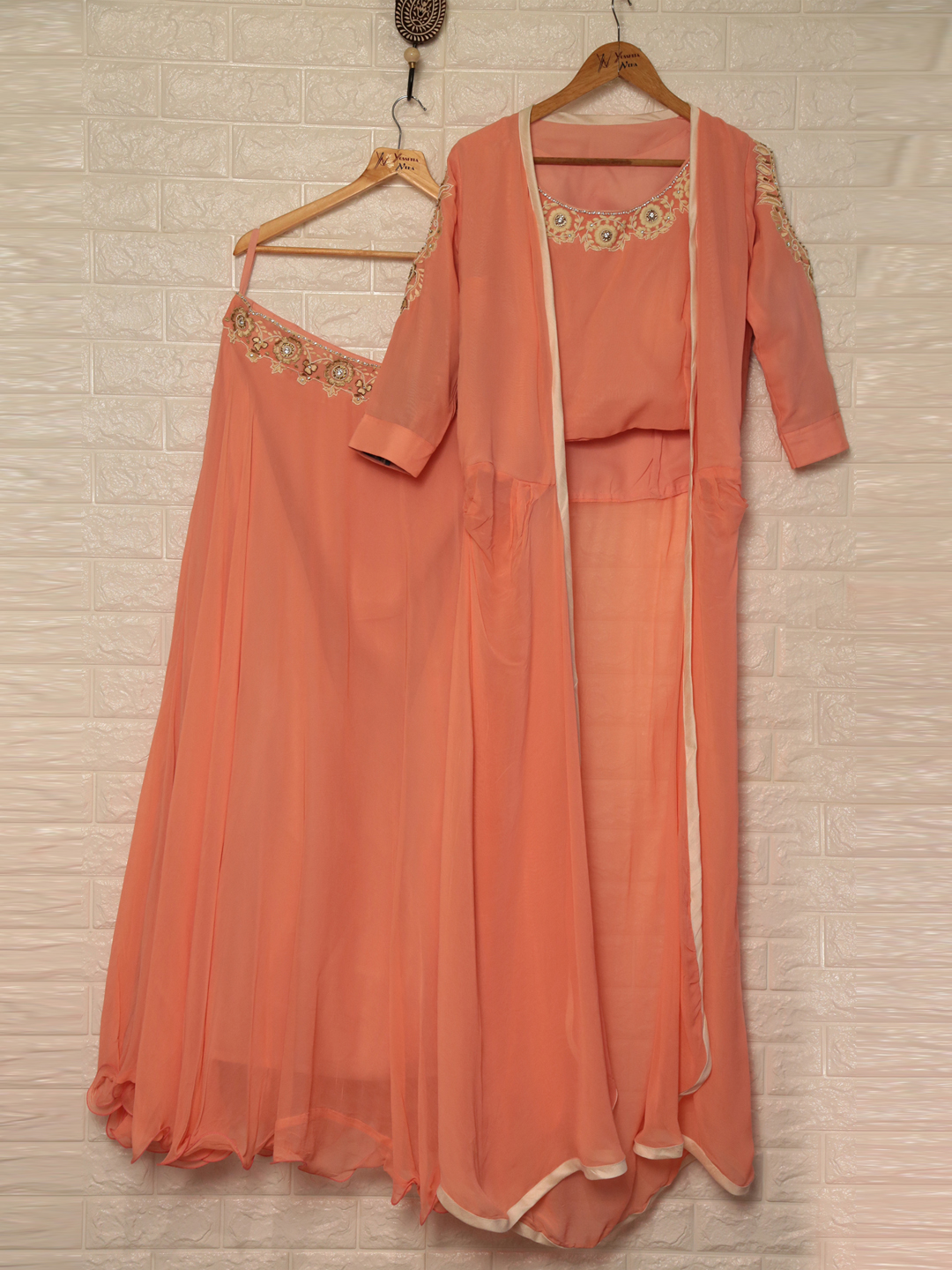 Peach traditional Indian outfit on hangers: embroidered neckline, sheer flowing dupatta, and matching pants against a white tiled wall.