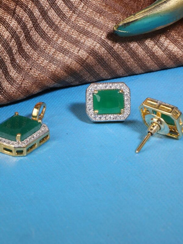 Gold jewelry set with square emerald-cut green stones, diamond halos, includes pendant and stud earrings on a blue surface.