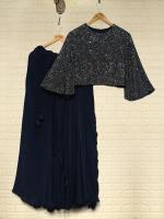 Two dresses on hangers: a floor-length navy gown and a black sequined cropped top with a matching skirt hanging side by side on a wall.