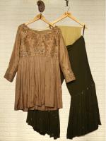 Two women's garments on hangers: a brown lace-trimmed tunic with three-quarter sleeves and a black skirt on the right on a beige wall.